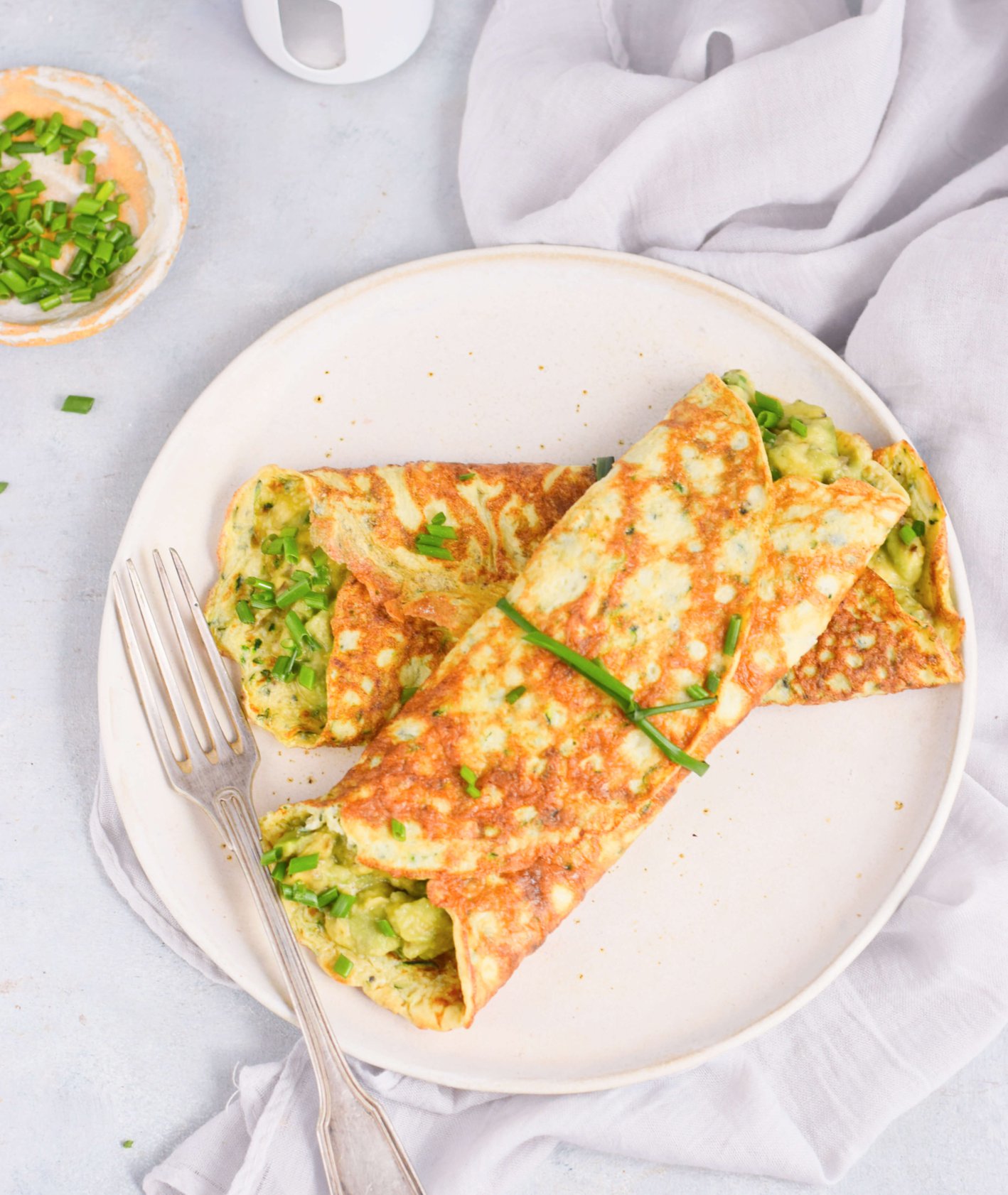 Talerz z omletami cukiniowymi z pastą z awokado, posiekany szczypiorek, solniczka, sztućce i ściereczka (fot. Anna Szewczyk)
