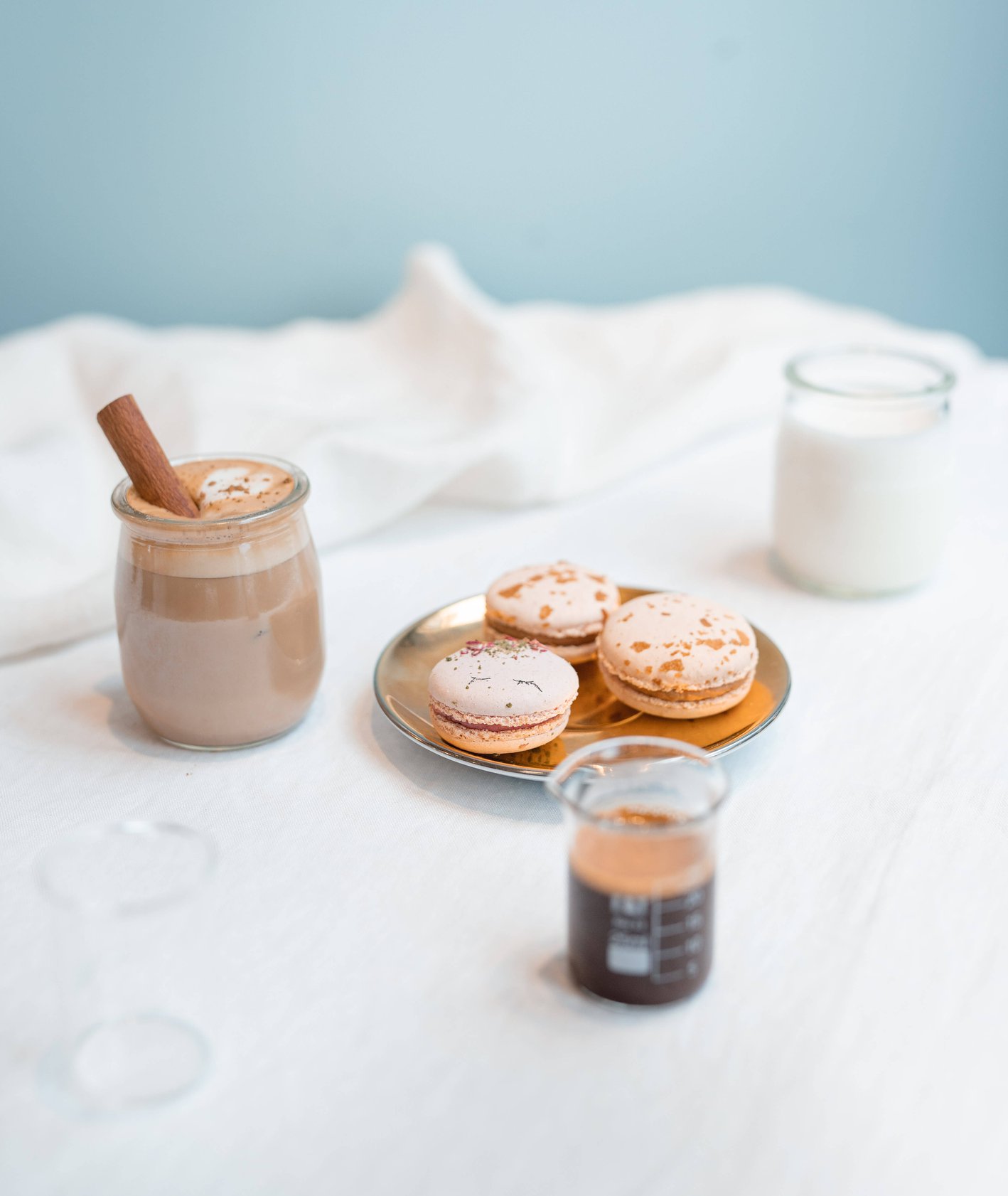 Cappuccino z cynamonem, makaroniki, mleko i espresso na białym obrusie (fot. Martyna Cybuch)